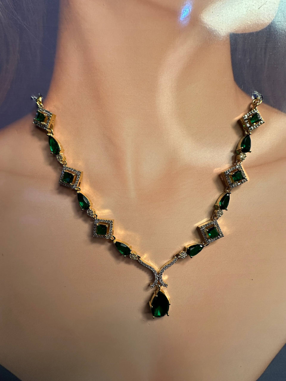 A gold-tone necklace with green marquise and square-cut stones, displayed on a mannequin bust.