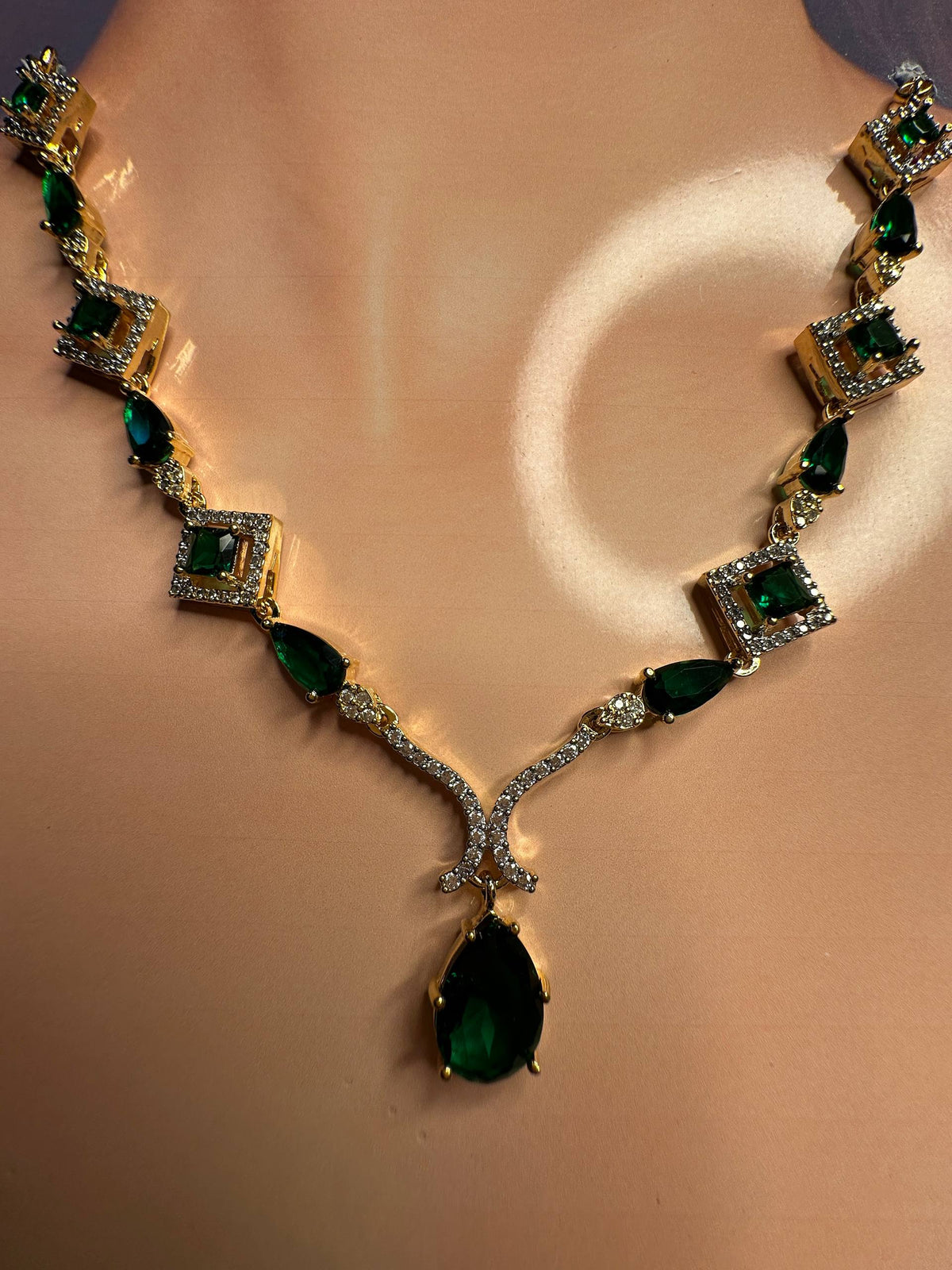 A gold-plated necklace with emerald-cut and marquise-cut green gemstones, displayed on a mannequin bust.