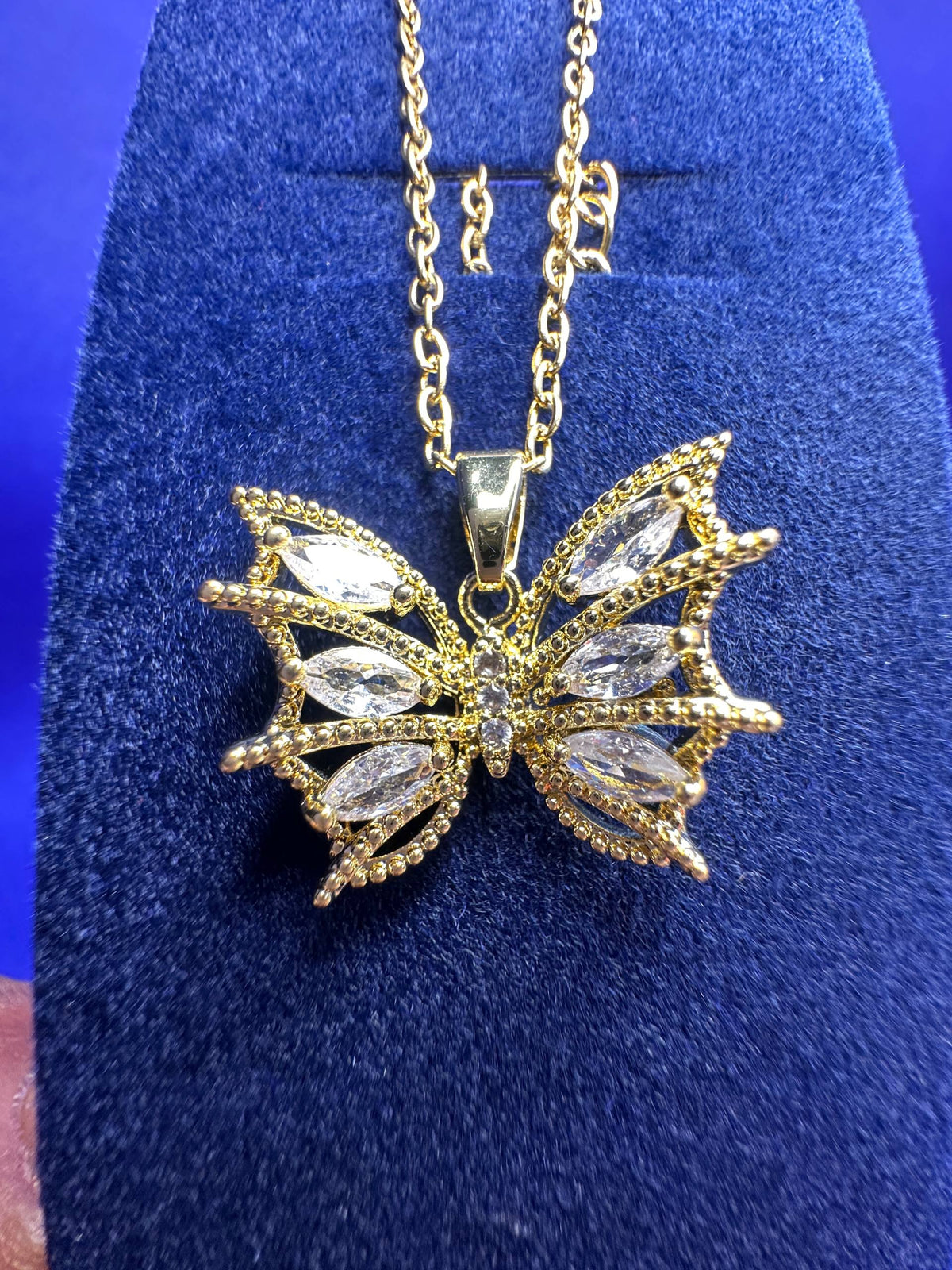 Gold butterfly pendant necklace with marquise-cut clear crystals, displayed on a blue velvet jewelry stand.